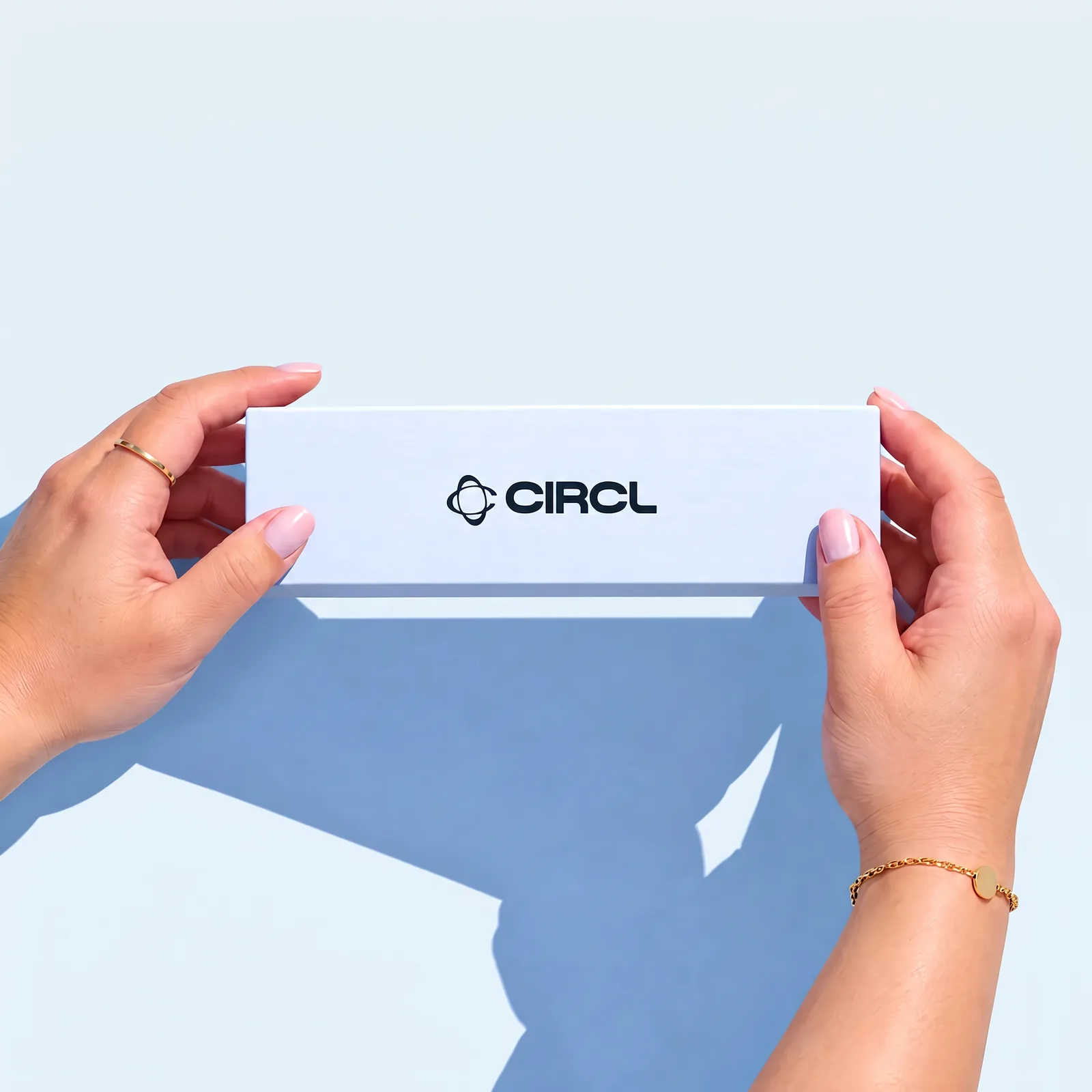 Two hands holding a white CIRCL box level against a pale blue background